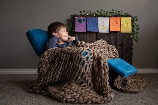 Creative Highlights Symbolbilder Boy lounging in cozy chair, with chunky blanket, and child-drawn art Norman, Oklahoma, United States CR_AOVS241025F-1567869-01 ,model released, Symbolfoto