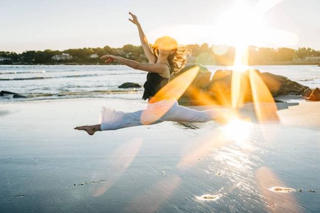 Creative Highlights Symbolbilder Woman performing a split leap on beach with vibrant sun flares Gloucester, Massachusetts, United States CR_FKNH241030-1571773-01 ,model released, Symbolfoto