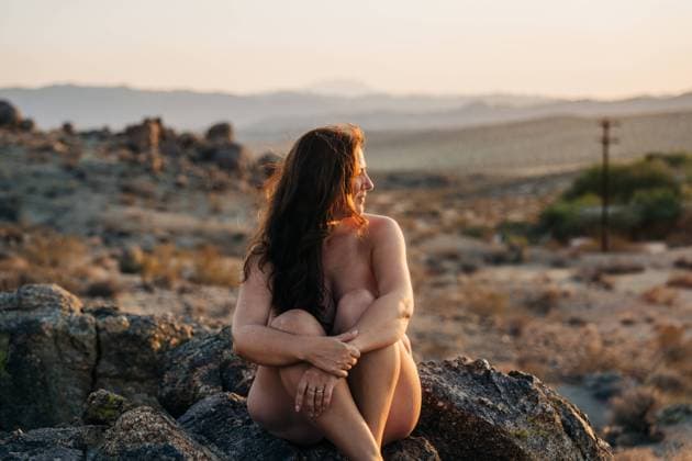Creative Highlights Symbolbilder Woman seated on desert rocks at sunset, gazing into the distance Joshua Tree, California, United States CR_FKNH241031B-1575556-01 ,model released, Symbolfoto
