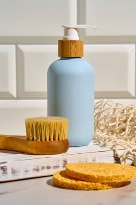 A matte blue cosmetic jar with a wooden lid, accompanied by natural spa accessories such as a wooden brush, two sponges and a woven net, neatly arranged on a white countertop Model Released Ikvyatkovskaya_ID24929_722257_001 Copyright: xIkvyatkovskayax