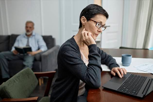 Woman paying bills on laptop while her husband reading book at home model released, Symbolfoto property released, KPEF00358