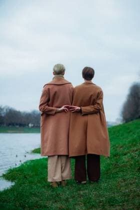 Creative Highlights Symbolbilder The two sisters in brown coats stand by a riverside, holding hands, against a cloudy sky 26331384 ,model released, Symbolfoto RECORD DATE NOT STATED