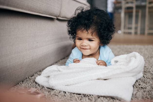 Creative Highlights Symbolbilder 783449156 Home, happy baby and playing with blanket for comfort, security and child development on carpet. Smile, infant and relax with growth, learning and mobility in living room for motor skills and posture. model released property released Copyright: xwww.peopleimages.comx
