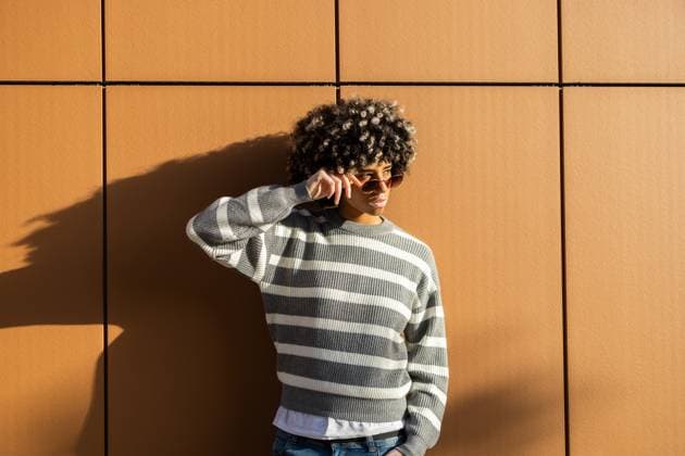 Creative Highlights Symbolbilder 783449156 A mixed race woman with vitiligo relaxes against a warm-toned wall on a sunny day at a university campus, wearing a striped sweater and sunglasses, exuding confidence and style Model Released DavidMunoz_ID25207_729190_061 Copyright: xDavidxMunozx