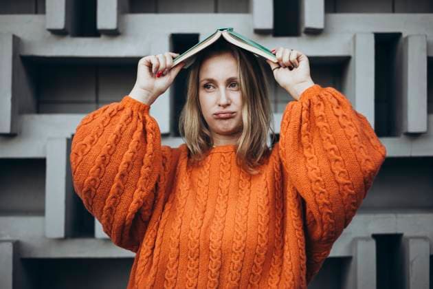 Creative Highlights Symbolbilder A female student in an orange sweater holds a book on her head while posing against a modern geometric wall The scene conveys a playful and creative atmosphere Model Released HannaYakimenko_ID25073_726378_009 Copyright: xHannaxYakimenkox RECORD DATE NOT STATED