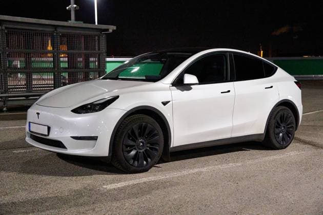 Augsburg, Bavaria, Germany - December 5, 2024: A white electric car, Tesla Model Y, parked in an open parking lot at night in the dark. The scene shows a car in everyday use with lighting and parking structure in the background.