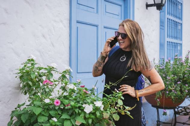 Creative Highlights Symbolbilder 783449156 Eine fröhliche Frau mittleren Alters mit glattem Haar und einer kurvenreichen lateinamerikanischen Figur plaudert am Telefon vor einer leuchtend blauen Kolonialtür. In einem eleganten schwarzen Kleid und mit Sonnenbrille strahlt sie Charme und Selbstbewusstsein aus A joyful middle-aged woman with straight hair and a curvy Latin figure chats on the phone in front of a vibrant blue colonial door. She exudes charm and confidence in a stylish black dress and sunglasses. Copyright: imageBROKER MariaxDanielaxRomero ibxktg11898077.jpg ,model released, Symbolfoto ,property released