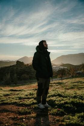 Creative Highlights Symbolfotos A young man in a hoodie stands in a sunlit field with mountains in the background, under a dramatic sky. 27727204 ,model released, Symbolfoto RECORD DATE NOT STATED