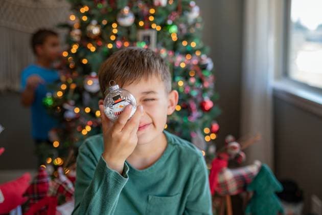 Boy holding a snowman ornament in front of eye by Christmas tree Norman, Oklahoma, United States R_AOVS241222-1601138-01 ,model released, Symbolfoto