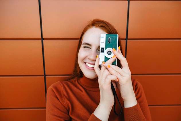 Smiling woman photographing with camera in front of brown wall model released, Symbolfoto, ALKF01406