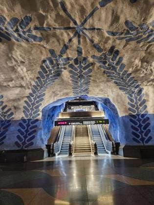 Creative Highlights World Artistic Stockholm metro station interior with blue and beige patterns on cave-like walls, featuring an escalator and vibrant lighting. 27920248