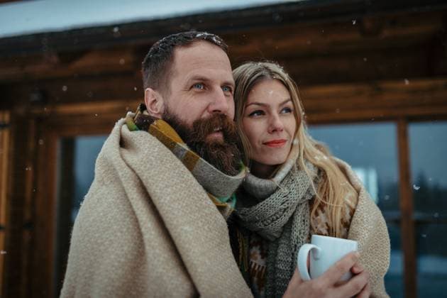 Couple bundled in thick blanket standing outdoor, hugging in front of a cabin during snowfall. Couple bundled in thick blanket standing outdoor, hugging in front of cabin during snowfall. model released