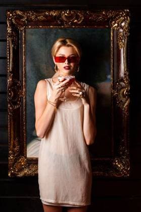 Creative Highlights Symbolbilder Stylish young woman in red sunglasses and a sheer dress holding a cocktail, framed by an ornate picture frame, against a dark background. 28318445 ,model released, Symbolfoto RECORD DATE NOT STATED