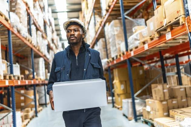Konzentrierter afrikanischer männlicher Arbeiter, der eine Kiste durch ein Auslieferungslager trägt Concentrated african male worker carrying a box along a distribution warehouse Copyright: imageBROKER UnaixHuizi ibxuhu12125091.jpg ,model released, Symbolfoto ,property released
