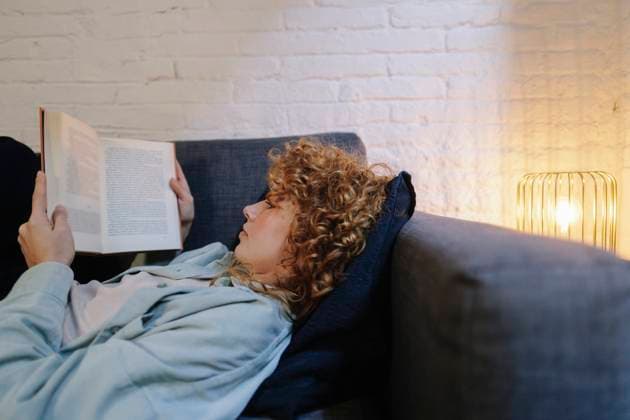 Curly hair woman reading book and lying on sofa at home model released, Symbolfoto property released, ASGF05993