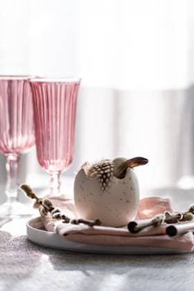 IMAGO Creative, Ostern, Bräuche, Osterbrunch A stylish Easter dining setup with a focal decorative egg adorned with feathers, nestled on a pastel tablecloth, complemented by elegant pink-tinted glasses. Model Released AnnaBogush_ID26004_750162_007 Copyright: xAnnaxBogushx RECORD DATE NOT STATED
