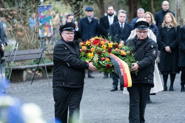 Aschaffenburg, Bavaria, Germany - January 26, 2025: Memorial service wreath-laying ceremony in Schöntal Park after knife attack in Aschaffenburg. Police officers carry two large wreaths - one in blue and white with the ribbon of the Bavarian Minister President and one in orange and red with the ribbon of the Thuringian police - to the memorial site. Nancy Faeser, Markus Söder and other mourners stand in the background. *** Gedenkfeier Kranzniederlegung im Schöntal Park nach Messerangriff in Aschaffenburg. Polizeibeamte tragen zwei große Kränze einen in Blau-Weiß mit der Schleife des bayerischen Ministerpräsidenten und einen in Orange-Rot mit der Schleife der Thüringer Polizei zur Gedenkstelle. Im Hintergrund stehen Nancy