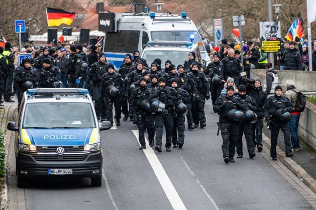 Aschaffenburg, Bavaria, Germany - January 26, 2025: Demonstration in Aschaffenburg due to knife attack. A large group of heavily equipped police officers march in formation at a demonstration, accompanied by emergency vehicles. The officers secure the area while demonstrators with banners and flags stand at the side of the road. *** Demonstration in Aschaffenburg wegen Messerangriff. Eine große Gruppe von schwer ausgerüsteten Polizeikräften marschiert in Formation bei einer Demonstration, begleitet von Einsatzfahrzeugen. Die Beamten sichern den Bereich, während Demonstranten mit Transparenten und Fahnen am Straßenrand stehen.