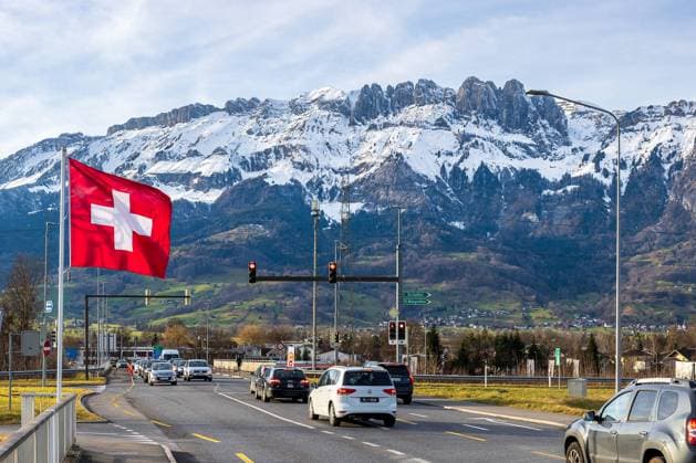 Grenzübergang Rheinbrücke Haag Bendern: Einreise von Liechtenstein in die Schweiz, 29.01.2025 Eine große Schweizer Fahne weht im Wind, während Autos an der roten Ampel auf die Einreise warten. Verkehrsschilder weisen nach St. Gallen und St. Margrethen. Im Hintergrund erheben sich die schneebedeckten Alpen über der grünen Landschaft. Klare Sicht und Sonnenschein prägen die Szene. Kanton St. Gallen Schweiz *** Border crossing Rhine bridge Haag Bendern Entering Switzerland from Liechtenstein, 29 01 2025 A large Swiss flag waves in the wind while cars wait at the red traffic light to enter the country Traffic signs point to St Gallen and St Margrethen In the background, the snow-capped Alps rise above the green landscape Clear views 20250129-6V2A7063-M4000