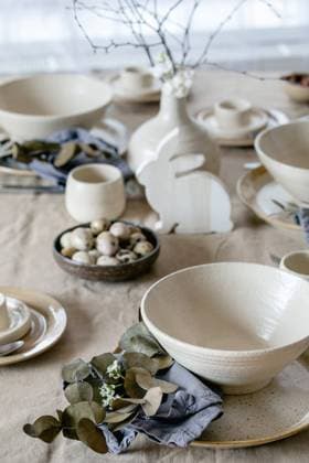 Gedeckter Ostertisch mit Keramikgeschirr Rustic Easter table setting with empty craft ceramic tableware, plates and bowls, Easter bunny rabbit decorations, branches in vase on linen tablecloth in front of the window. Easter holiday dinner. Copyright: xZoonar.com NATASHAxBREENx 22727483