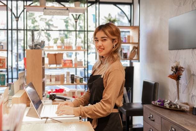 IMAGO Creative, Naturkosmetik A cosmetics store employee stands by a counter using a laptop, surrounded by skincare products. The modern retail space is filled with natural light and organized displays. Model Released DavidMunoz_ID26443_762994_013 Copyright: xDavidxMunozx