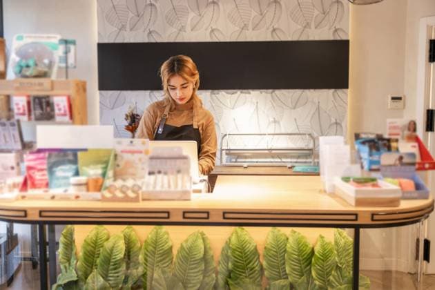 IMAGO Creative, Naturkosmetik Female employee stands behind the counter of a cosmetics store, surrounded by beauty products. The store features a modern interior with leafy decorations. Model Released DavidMunoz_ID26443_762995_014 Copyright: xDavidxMunozx