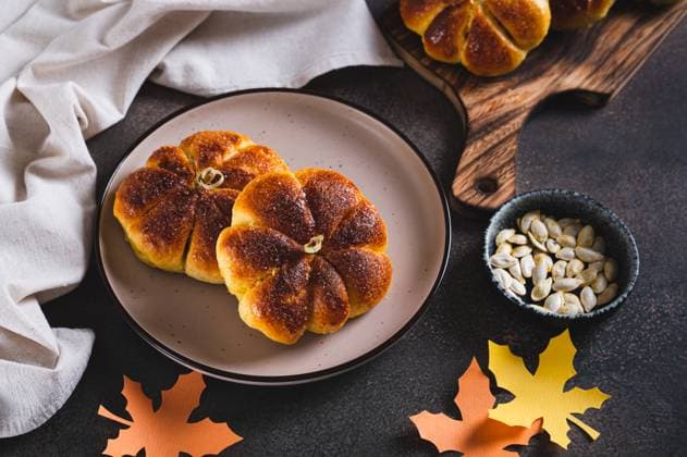 Herbstliche kürbisförmige Brötchen mit Zucker bestreut auf einem Teller auf einem Tisch Autumn pumpkin shaped bread buns sprinkled with sugar on a plate on a table Copyright: xZoonar.com ElenaxRuix 22810838
