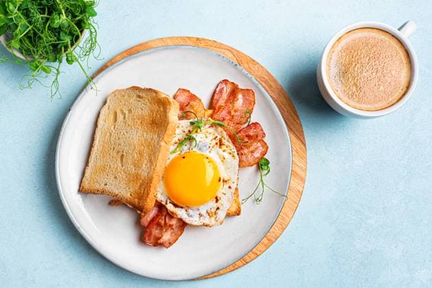 Frühstückssandwich mit Spiegelei, Speck und Sprossen Breakfast sandwich with fried egg, bacon and green pea sprouts on blue background. Fried sunny side egg with bacon on toast with microgreens and morning cappuccino coffee. Healthy breakfast. Copyright: xZoonar.com OksanaxBratanovax 22830818