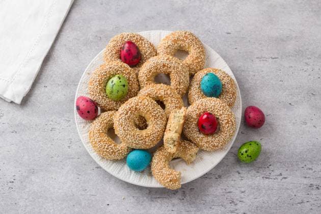 Weißer Teller mit traditionellem griechischem Ostergebäck Koulourakya oder Koulourya Mürbeteigringe mit Sesam, verziert mit bunten Eiern auf grauem, strukturiertem Hintergrund. Hausgemachtes Ostergebäck White plate with traditional Greek Easter cookies Koulourakya or Koulourya shortbread rings with sesame seeds, decorated with colored eggs on a gray textured background, top view. Homemade Easter pastries. Copyright: xZoonar.com OlgaxLepeshkinax 22857105