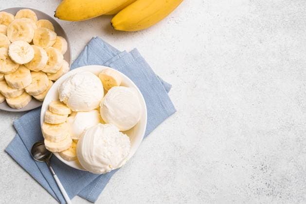 Bananeneis und Bananen Ice cream scoops and banana slices in bowl on white background, top view, copy space. Healthy raw vegan banana ice cream (nicecream), homemade organic dessert, dairy free, gluten free. Copyright: xZoonar.com OksanaxBratanovax 22892272