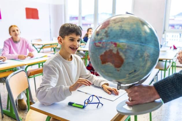 Lehrerin zeigt einem lächelnden Schüler während einer Geografiestunde in der Grundschule den Planeten Erde auf einem Globus Teacher showing planet earth on a globe to a smiling student during a geography lesson in elementary school classroom Copyright: imageBROKER UnaixHuizi ibxuhu12678425.jpg ,model released, Symbolfoto ,property released