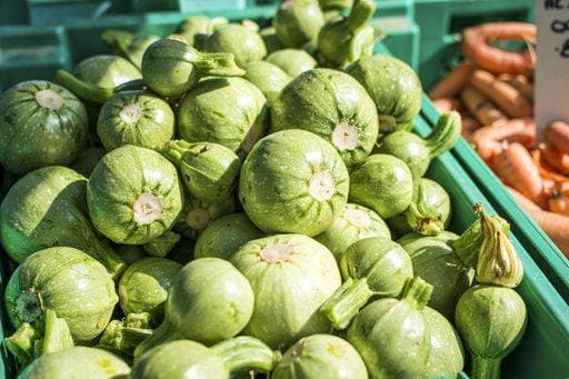 Fresh round zucchinis displayed in a green crate at a vibrant farmers market, capturing the essence of local produce. 28945542 RECORD DATE NOT STATED