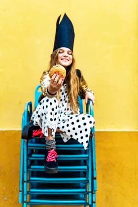 Creative Highlights Symbolfotos Smiling girl wearing black crown sitting on stack of chairs holding hamburger model released, Symbolfoto, ERRF00906