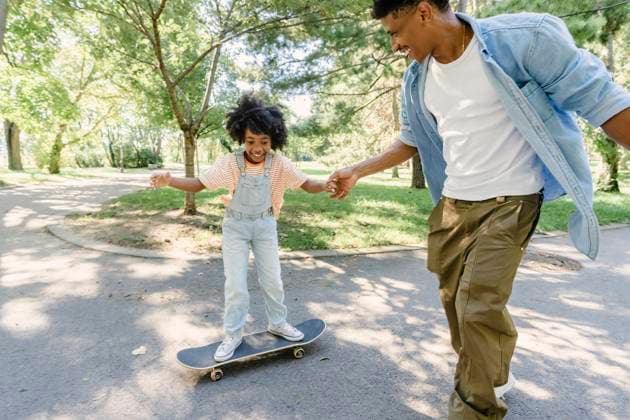 Happy young man holding hand of daughter skating on footpath in garden model released, Symbolfoto, AAZF02152