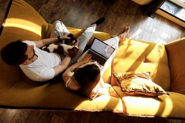 IMAGO Creative, Lifestyle, Gaming A woman works on her laptop while a man plays a console with a dog on his lap in a living room model released, Symbolfoto property released, EHAF00440