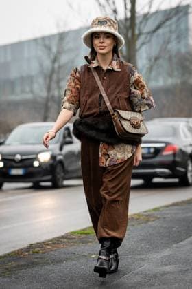 Street Style at Milan Fashion Week 2025 - Gucci in Milan, Italy on 25 February 2025 Street Style: A guest wears light brown Gucci monogram sherpa lined Gucci bucket hat, gold earrings, light gray dark orange bear pattern short sleeve oversized shirt, dark brown suede zipped vest, shiny dark brown Gucci monogram leather bag, dark brown baggy pants, shiny black Gucci silver chain boots leather shoes outside of the Gucci fashion show during the Milan Fashion Week Womenswear Fall Winter 2025 2026 in Milan, Italy on 25 February 2025., Credit:Stefano Costantino TTL Avalon Milan, Italy Copyright: xStefanoxCostantinoxTTLx xAvalonx 0968952543