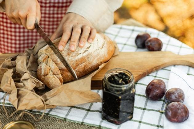 IMAGO Creative, Jahreszeit Sommer, Food, Pflaume Hands slicing rustic bread on a wooden board, surrounded by fresh plums and jam. An inviting scene for preparing delicious homemade canapes in a cozy kitchen setting. Model Released Ptashkimenko_ID26208_756096_006 Copyright: xPtashkimenkox