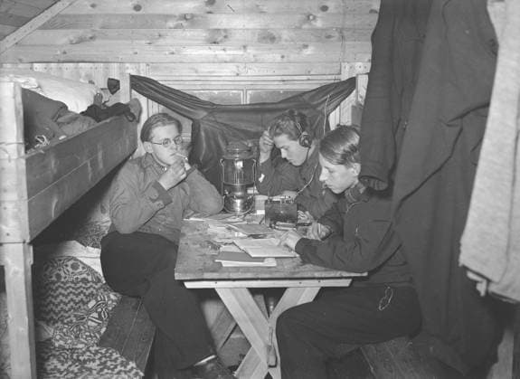 In der Zeit des Zweiten Weltkriegs. Der Krieg erschwerte die Einfuhr von Kohle zum Heizen von Häusern und Wohnungen. Anstelle von Kohle musste Holz verwendet werden. In großen Städten wie Stockholm konnte man große Holzstapel entlang der Straßen sehen. Viele Männer bekamen befristete Jobs, um das Holz zu hacken. Hier sind zwei junge Männer zu sehen, die in den Wäldern außerhalb der västmanischen Stadt Skinnskatteberg arbeiten. Sie machen eine dringend benötigte Pause in ihrer einfachen Hütte, in der es keinen Strom gibt. Auf dem Tisch brennt eine Primus Kerosinlaterne. Einer der Männer hört über Kopfhörer in einen Kristallempfänger. Ein früher Typ von Radioempfänger, bevor Radios Elektronenröhren und Lautsprecher hatten. Der Kristallempfän Copyright: imageBROKER Sjoberg ibljsj12852787.jpg