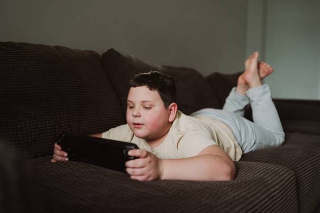 Creative Highlights Symbolfotos Young boy lying on a comfortable brown sofa, fully immersed in a hand held video game console. The cozy home environment reflects a relaxed leisure time. Model Released JenyKulikova_ID26998_779233_025 Copyright: xJenyxKulikovax