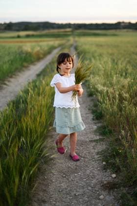 Creative Highlights Symbolfotos MR_ID27203_20165_MayaBosquetCarli.jpg, MR_ID27203_20166_LeoBosquetCarli.jpg A young girl in a white blouse and green skirt walks a dirt path, holding stalks of wheat. The calm rural scene, set at sunset, portrays a quaint and serene moment. Model Released MagdalenaCarli_ID27203_782326_001 Copyright: xMagdalenaxCarlix
