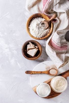 Sourdough for baking bread Rye and wheat sourdough in glass jars, fresh and instant yeast, olive wood bowl of flour for baking homemade bread. With spoon, serving board, kitchen towel over gray concrete background. Top view Copyright: xZoonar.com NatashaxBreenx 23041975