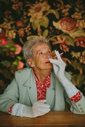 Creative Highlights Symbolfotos An elderly woman in a vintage setting, wearing elegant attire, looks thoughtfully with a pink candle. The floral background adds to the nostalgic and classic vibe. Model Released CamilleGirard_ID26984_778927_026 Copyright: xCamillexGirardx RECORD DATE NOT STATED