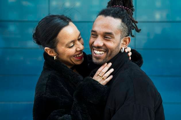Creative Highlights Symbolfotos A happy multicultural couple embraces and smiles lovingly at each other, symbolizing joy and connection. They are wearing black coats against a modern blue background. Model Released LuciaVargas_ID27837_799266_010 Copyright: xLuciaxVargasx