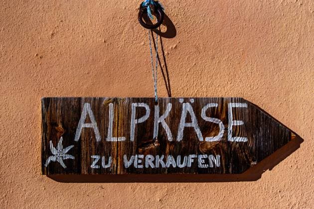 Holzschild mit der deutschen Aufschrift Alpkäse zu verkaufen vor einer rosa Hauswand. Hinweis auf den Direktverkauf von Schweizer Alpkäse auf der Alp. *** Wooden shield with the Germans Inscription Alpine cheese to sell before a Pink House wall Note at the Direct sales from Swiss Alpine cheese at the Alp 1133300007