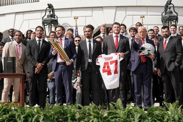 President Trump holds a helmet gifted to him by the 2025 College Football National Champions - The Ohio State University as Vice President JD Vance holds the top of the team trophy after he dropped the base on the South Lawn of the White House in Washington, DC on Monday, April 14, 2025.  WAS20250414586 KenxCedeno