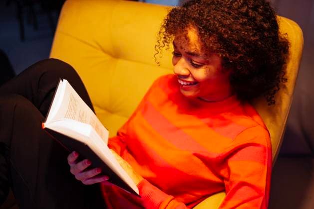 Junge lachende afrikanische Frau im Pullover sitzt im gelben Sessel und liest. Sorgloses Mädchen hält ein Buch und entspannt sich im Wohnzimmer. Young laughing African woman in sweater is sitting in yellow armchair and reading. Attractive black girl is smiling and relaxing at home. Carefree girl is holding book and relaxing in living room (License=RF) ,model released, Symbolfoto Copyright: xZoonar.com DashaxPetrenkox 23166938 ,model released, Symbolfoto ,property released