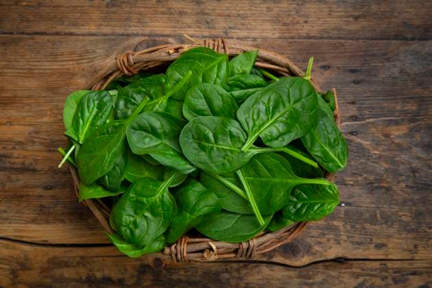 Fresh baby spinach in a willow basket on a wooden background, LVF09447