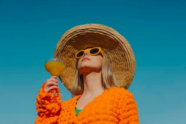 Stylish woman in orange clothing and straw hat enjoying a cocktail outdoors model released, Symbolfoto, VSNF03025