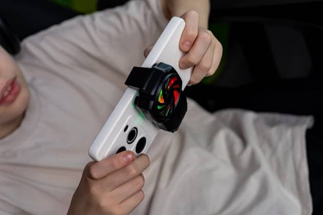 IMAGO Creative, Lifestyle, Gaming Teen boy intensely focused on mobile gaming, holding a smartphone with a cooling fan. The setup enhances gameplay experience and performance during intense sessions Model Released Ikvyatkovskaya_ID28180_830165_031 Copyright: xIkvyatkovskayax RECORD DATE NOT STATED