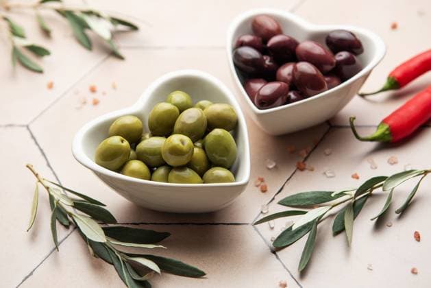 Herzförmige Schalen mit grünen und schwarzen Oliven, Olivenzweigen, Chilischoten und Himalayasalz auf gefliester Oberfläche Green and black olives served in heart shaped bowls, decorated with olive tree branches, chili peppers and himalayan salt, creating an elegant and appetizing presentation (License=RF) Copyright: xZoonar.com OlenaxRudox 23386901